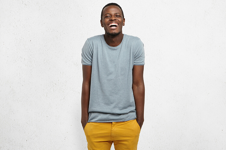 Een jonge man die breed lachend tegen een muur staat.