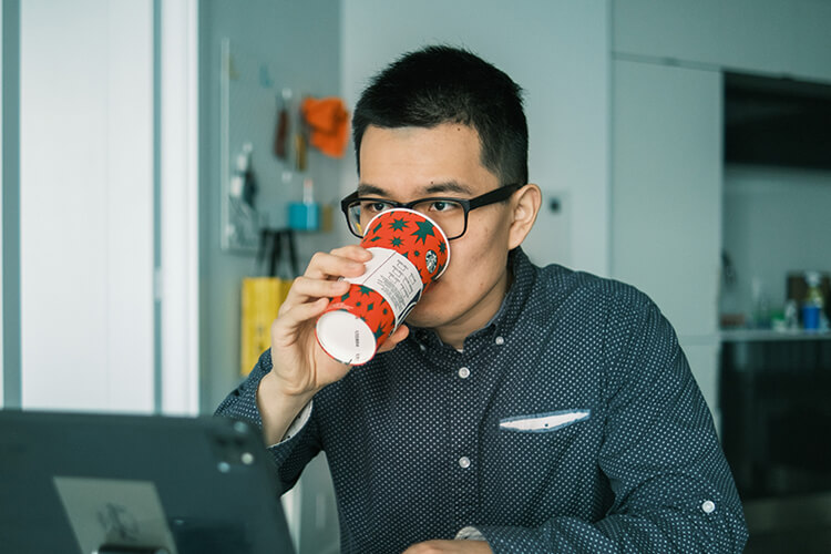 Man drinkt uit een beker terwijl hij werkt achter een laptop